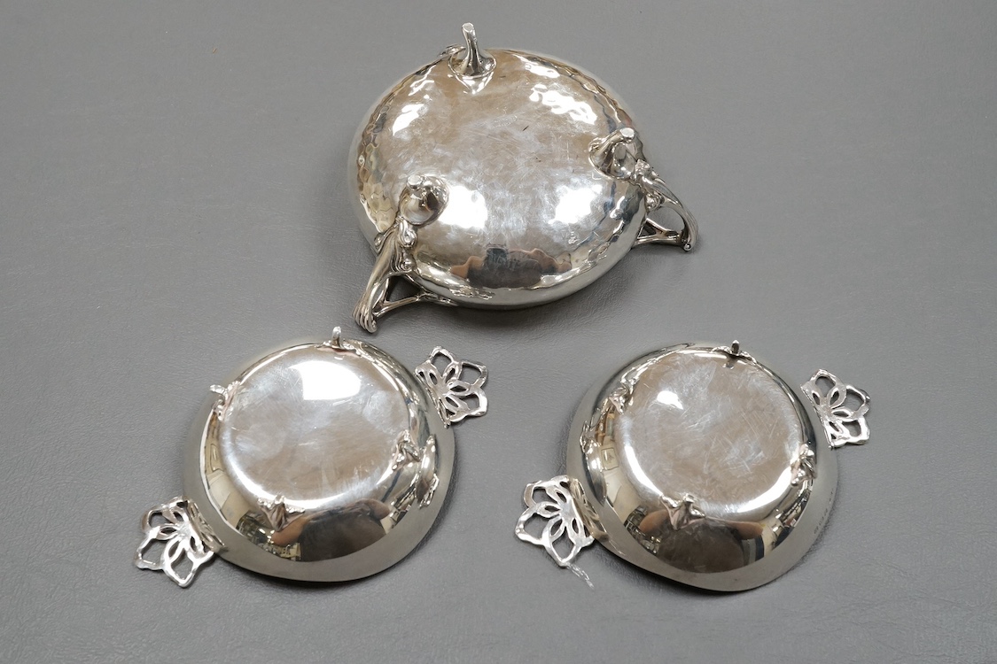 An Edwardian Art Nouveau planished silver tri-handled bowl by Charles Edwards, London, 1905, with stylised handles, diameter 94mm excluding handles, together with a pair of later silver two handled bonbon dishes, Deakin
